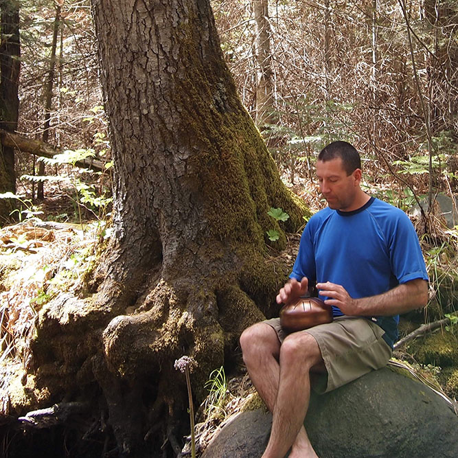 A man playing a steel tongue drum HAPI Drum in the forest